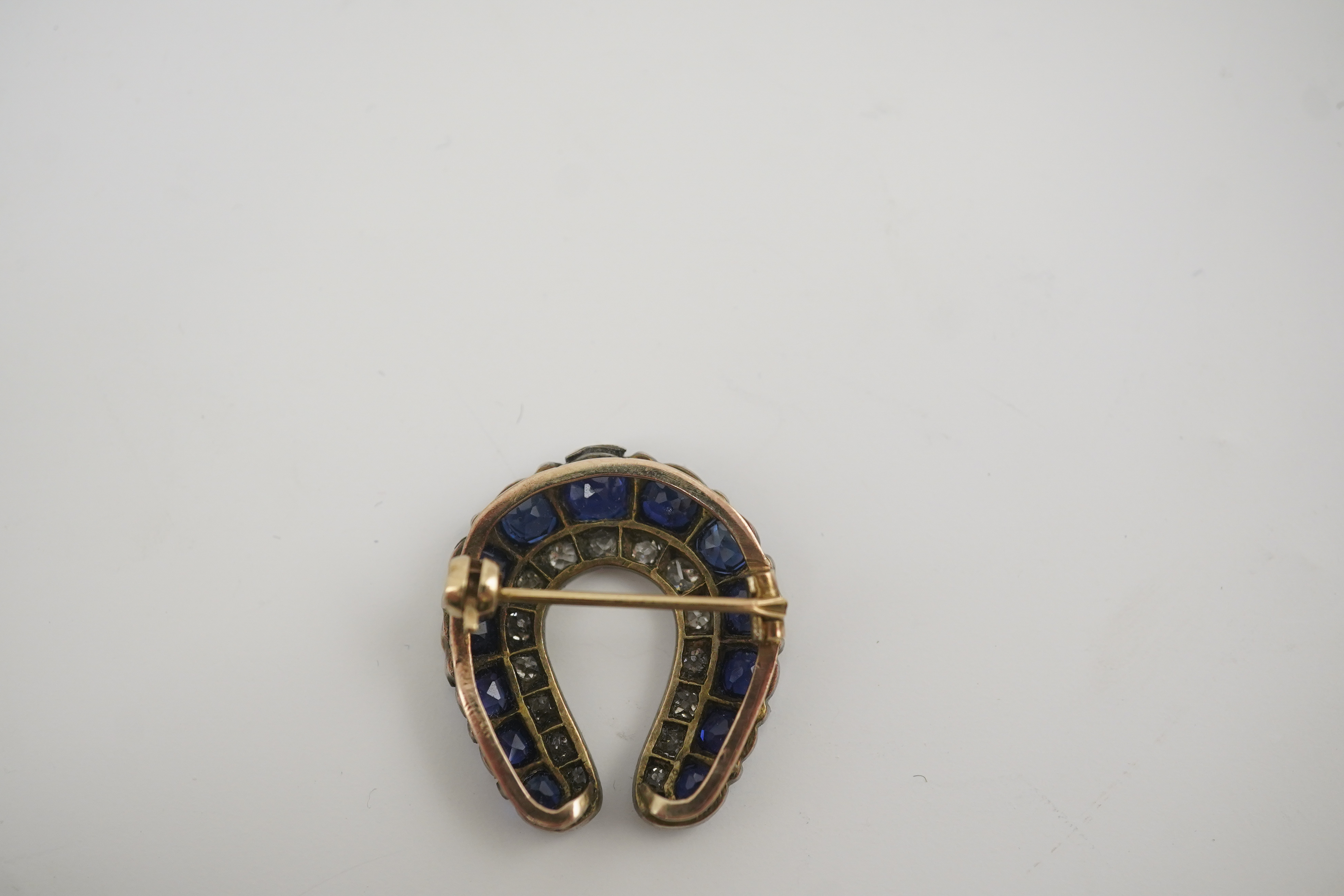 An Edwardian, gold and silver, diamond and sapphire set ‘horse shoe’ brooch